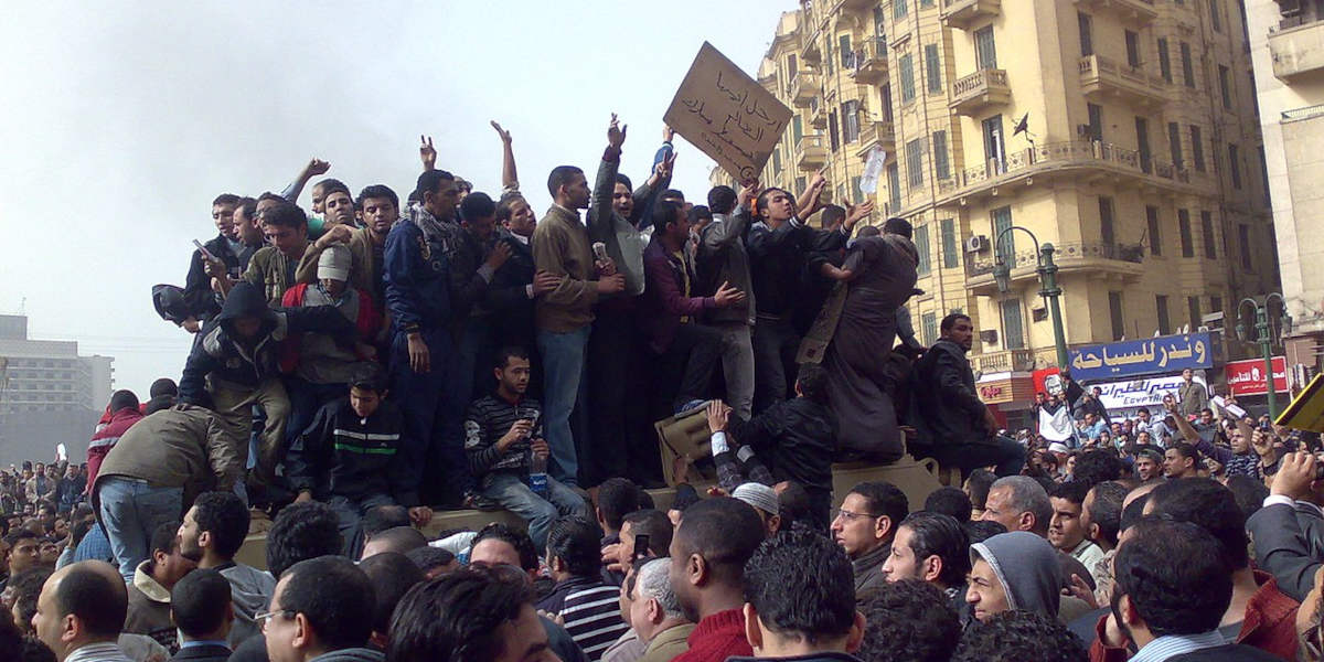 Protestors on top of an army truck holding signs and surrounded by a crowd