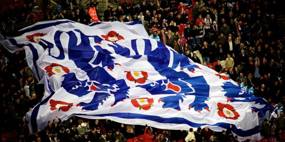 A crowd in a stadium holds up a huge Three Lions flag