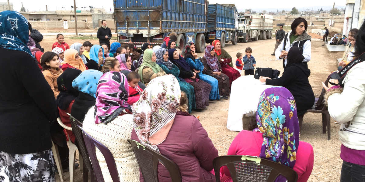 A group of women with several children sat in a semi-circle with a table at the centre