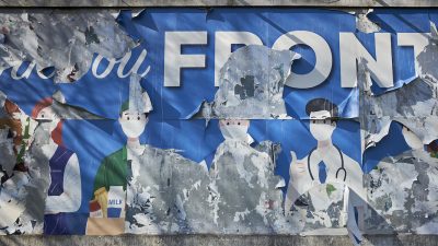 A torn billboard poster showing key workers in face masks