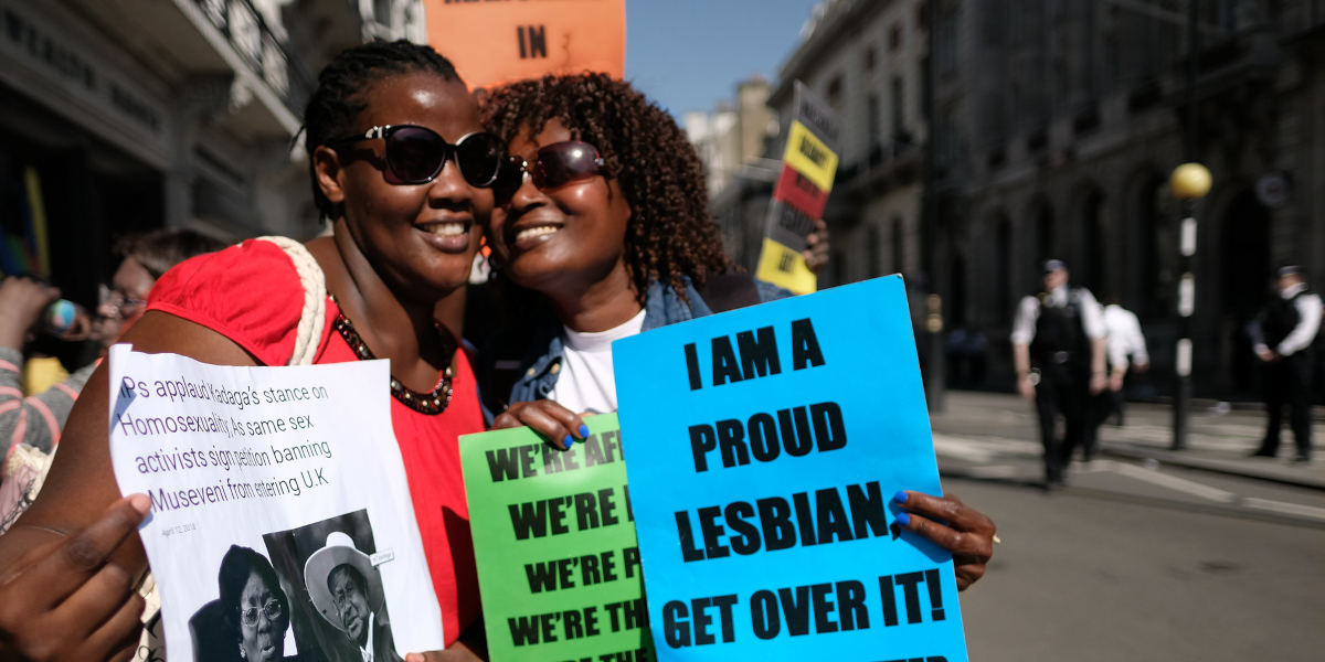 Two Black women hold up signs protesting anti-lgbtq laws, one reading "I am a proud lesbian, get over it!"