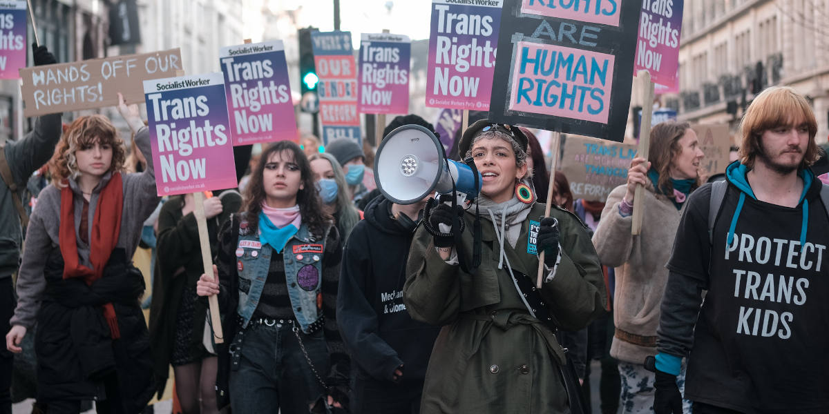 Protestors in London holding pro-trans rights placards, with one in the centre holding a megaphone