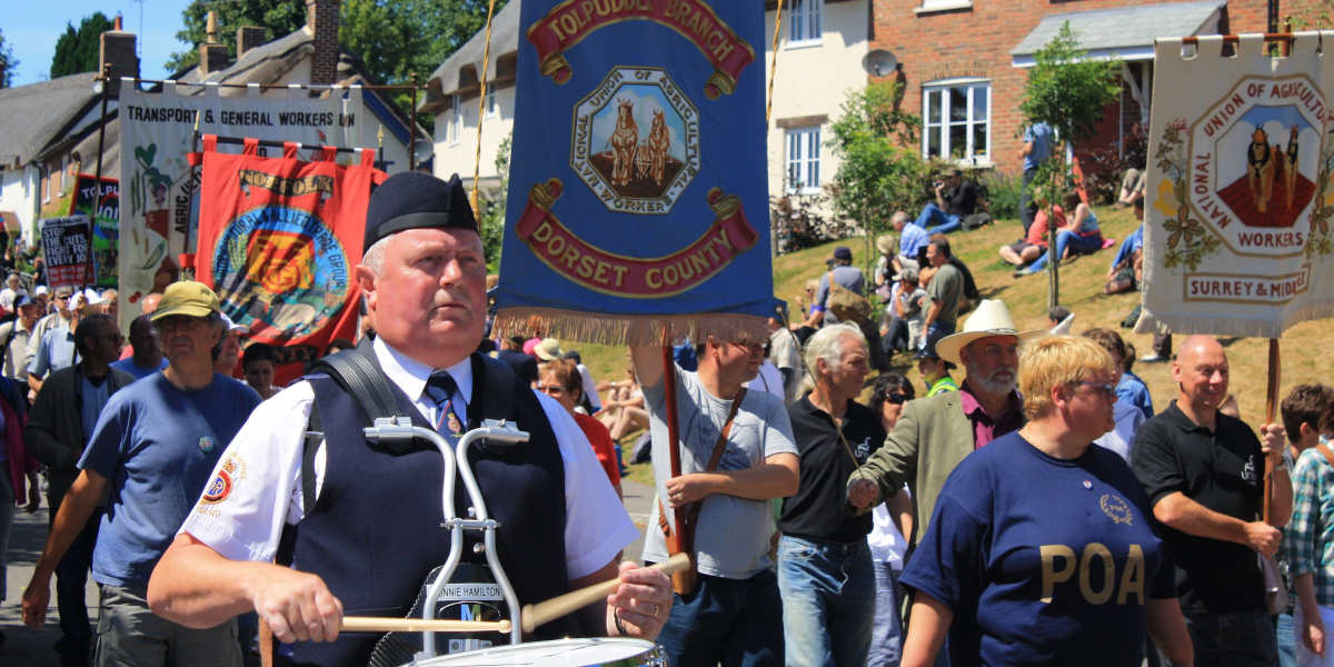 A procession carrying banners representing different British trade unions, with a drummer in the foreground