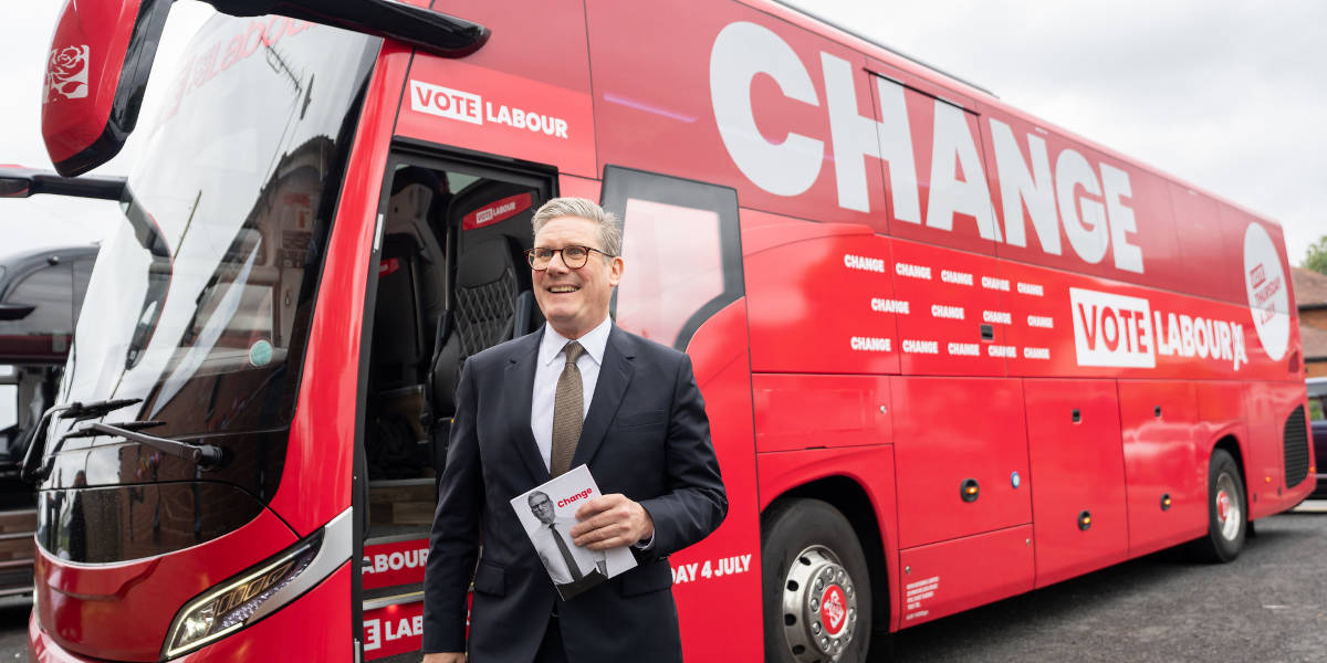 Keir Starmer holds a copy of the Labour manifesto in front of a red bus with the word 'Change' pasted on the side