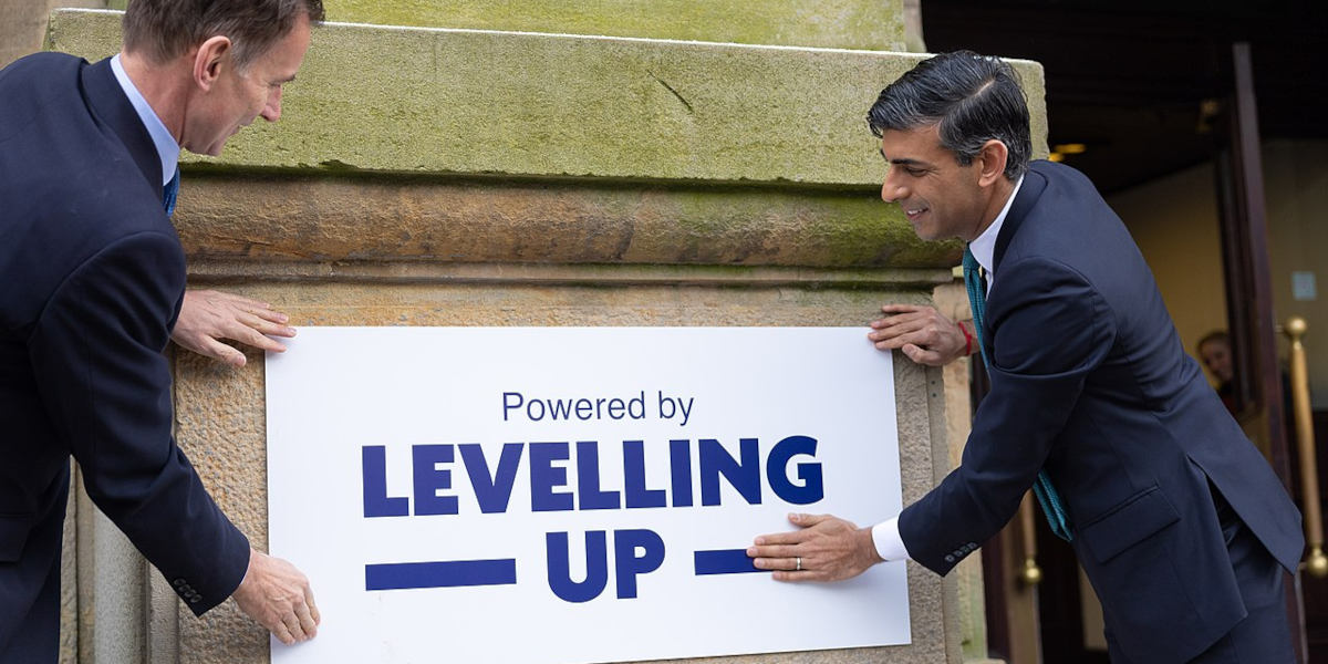 Former Prime Minister Rishi Sunak and former chancellor Jeremy Hunt placing a sign reading "levelling up" on a building